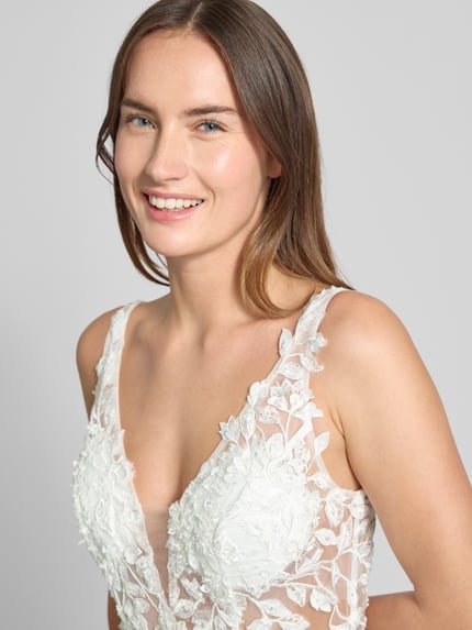 Modelka kobieca nosi Regular Fit Brautkleid mit floralem Spitzenbesatz od Luxuar, białe, półprzezroczyste, koronka, zbliżenie na górę sukni.