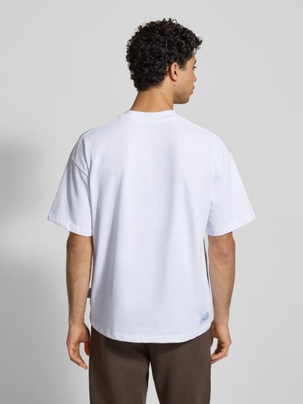 Männermodel trägt T-Shirt mit Label-Print von ANOTHER COTTON LAB in Weiß, Reine Baumwolle, Lockerer-Schnitt, Rückenlänge 73 cm, Ganzkörperansicht Rückansicht.