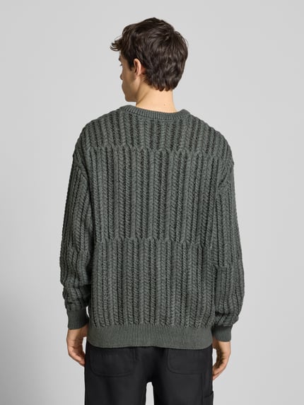 Männermodel trägt Relaxed Fit Strickpullover aus Baumwoll-Mix Modell 'FILL RLX' von Only & Sons in Unifarbe mit Zopfmuster, Ganzkörperansicht Rückansicht.