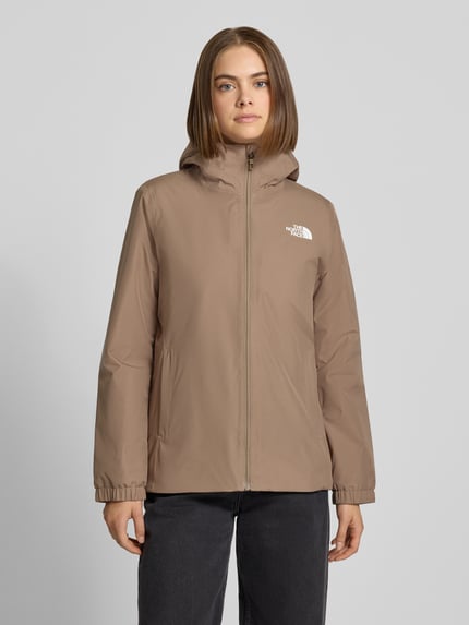 Frauenmodel trägt beżową kurtkę funkcyjną z nadrukiem z logo, krój regular fit, Model 'Quest Mono' od The North Face, Kaptur, zamek błyskawiczny, długość tyłu w rozmiarze S: 69 cm, szerokość ramion w rozmiarze S: 40 cm, szerokość klatki piersiowej w rozmiarze S: 40 cm, długość rękawów w rozmiarze S: 63 cm, Ganzkörperansicht von vorne.