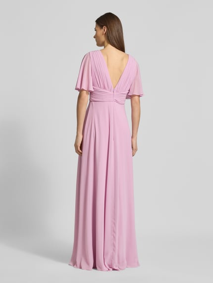 Modelka prezentuje Sukienka wieczorowa Regular Fit Abendkleid mit V-Ausschnitt von Jake*s Cocktail, szyfon, krój regular fit, dekolt w serek, efekt plisów, rękaw o dł. 1/2, dekolt na plecach, wszyty zamek błyskawiczny, nieprześwitująca halka, długość tyłu w rozmiarze 36: 126 cm, szerokość w rozmiarze 36: 40 cm, długość rękawów w rozmiarze 36: 29 cm, jasnoróżowy kolor, widoczne delikatne drapowania, gładka faktura, pełny widok sylwetki od tyłu