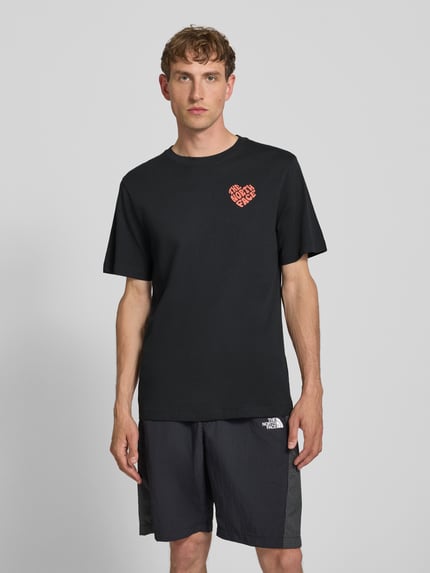 Männermodel trägt T-Shirt mit Label-Print und Rundhalsausschnitt von The North Face, schwarze Reine Baumwolle, Regular-Fit, Ganzkörperansicht von vorne. Rückenlänge bei Größe M: 74 cm.