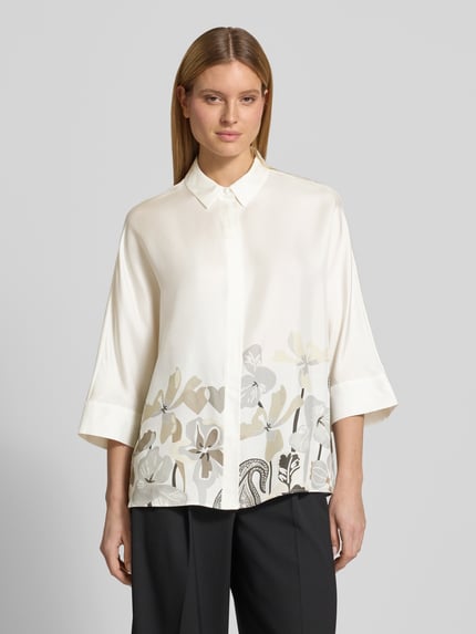 Modelka nosi Relaxed Fit Hemdbluse aus reiner Seide mit floralem Print von HERZENS, kremowe odcienie, gładka tekstura, kwiatowy nadruk, krój relaxed fit, kołnierzyk koszulowy, rękaw o dł. 3/4, listwa guzikowa, długość tyłu w rozmiarze 36: 73 cm, długość rękawów w rozmiarze 36: 43 cm, widok na cały przód.