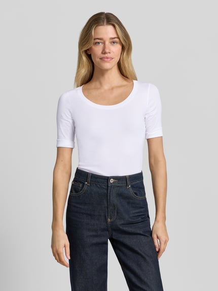 Kobiece modelka nosi T-Shirt mit Ärmelaufschlag und Rundhalsausschnitt von Marc Cain, mieszanka bawełny z dodatkiem streczu, dopasowany krój, okrągły dekolt, zakładki na rękawach, detal z logo, długość tyłu w rozmiarze 36: 60 cm, gładka biel, proste jeansy, gładka faktura, widok całej sylwetki z przodu.