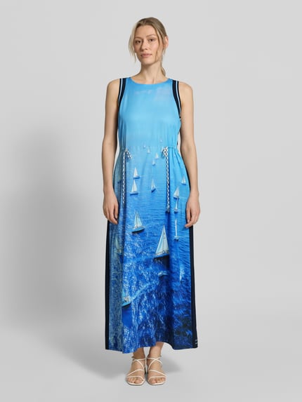 Vrouwenmodel draagt Maxikleid aus reinem Lyocell mit Allover-Foto-Print van Marc Cain, blauwe tinten, getailleerde pasvorm, ronde hals, mouwloos design, ruglengte maat 36: 134 cm, borstwijdte maat 36: 47 cm, all-over fotoprint met zeilboten, gladde textuur, voorkant volledig zichtbaar, geheel beeld, full-body van voren.