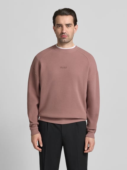 Männermodel trägt Regular Fit Sweatshirt aus reiner Baumwolle Modell 'DAFFLYN' von HUGO in Altrosa mit Strukturmuster, Ganzkörperansicht von vorne.