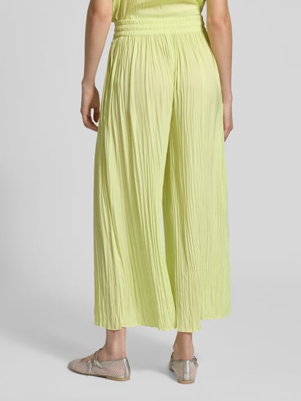 Frauenmodel trägt Pull-on-Hose mit Plisseefalten mit Tunnelzug von Marc Cain in hellem Gelb, elastischer Bund, Label-Detail, Relaxed-Fit, Ganzkörperansicht Rückansicht.