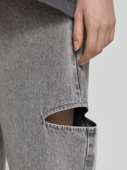 Frauenmodel trägt Mom Fit Jeans mit Cut Out von Karo Kauer aus Reine Baumwolle im 5-Pocket-Design, graue Textur, Nahaufnahme Oberschenkel.