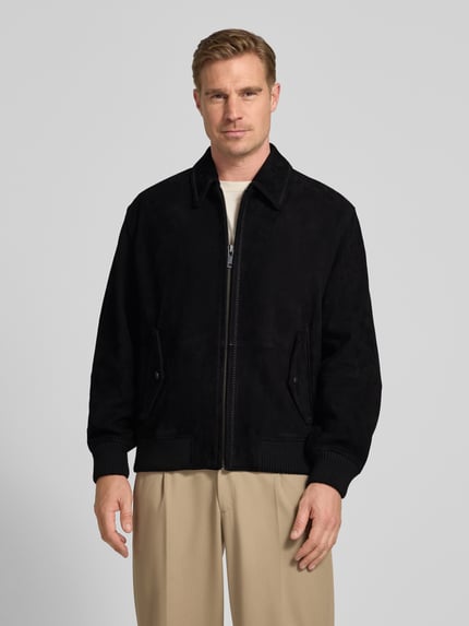 Męski model nosi Super Slim Fit Lederjacke aus Ziegenleder Modell 'Lemai' od HUGO, czarny kolor, wykładany kołnierz, imitacja skóry welurowej, długi rękaw, zamek błyskawiczny, kieszenie z patką, napis z logo, zakończenie rękawów i dołu prążkowane, skóra kozia, wykończenie materiału: skóra welurowa, Ganzkörperansicht von vorne.