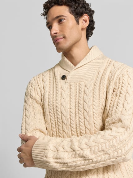 Männermodel trägt Strickpullover mit Zopfmuster Modell 'CALLUM' von JACK & JONES Premium, kremowy, bawełna, krój slim fit, szalowy kołnierz, guzik, Nahaufnahme Oberkörper.