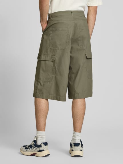 Mężczyzna nosi Straight Fit Shorts mit Cargo-Taschen Modell 'Camo' von KARL KANI z bawełny, wpuszczane kieszenie, kieszenie cargo, kieszenie z tyłu, zapięcie na guzik i zamek błyskawiczny, szerokość w rozmiarze M: 41 cm, długość wewnętrzna nogawki: 38 cm, kolor oliwkowy, widok całej sylwetki z tyłu.