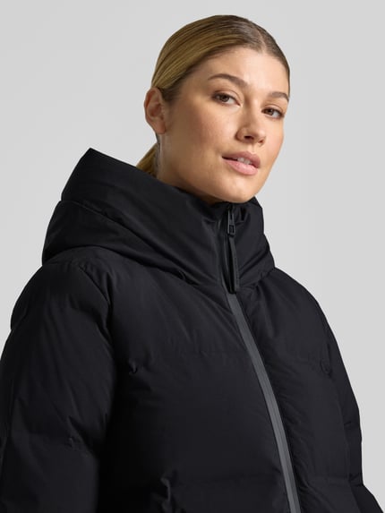 Frauenmodel trägt schwarze Regular Fit Daunenjacke mit abnehmbaren Rucksackgurten von Marc O'Polo, glatte Struktur, Nahaufnahme Oberkörper, Damen Daunenjacke von Marc O'Polo.
