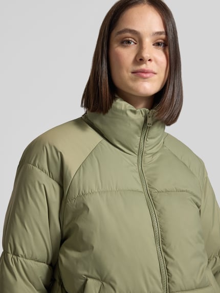 Frauenmodel trägt Pufferjacke mit Stehkragen Modell 'VMBRENDA' von VERO MODA in Olivgrün, Webware mit Steppeinsatz, Nahaufnahme Oberkörper.