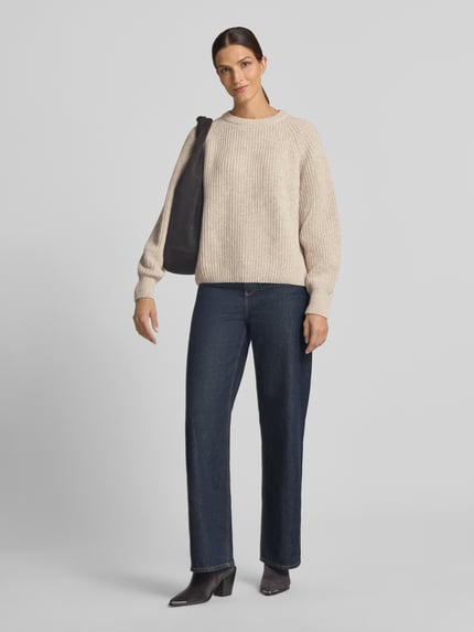 Modelka kobieta nosi beżowy sweter z mieszanki wełny Loose Fit Pullover aus Woll-Mix Modell 'RIB KNIT' od ARMEDANGELS, granatowe szerokie spodnie, czarne buty, czarna torba na ramieniu, widok całej sylwetki z przodu