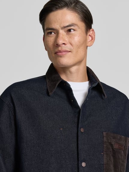 Männermodel trägt Overshirt mit Kentkragen in Cord-Optik und Label-Patch von Armani Exchange, dunkelblau und braun, Nahaufnahme Oberkörper, regular fit, met borstzak, sportmanchetten, ruglengte maat M 70 cm.
