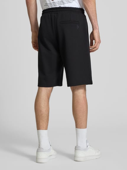 Männermodel trägt Shorts mit elastischem Bund und Ziernähten von REVIEW in Schwarz, Material-Mix mit Stretch-Anteil, Loose-Fit, Ganzkörperansicht Rückansicht.
