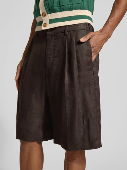 Mannelijk model draagt 'Leinenshorts aus reinen Leinen' van Drykorn in donkerbruin, los vallend, met knoop- en ritssluiting, voorzakken, achterzakken en plooien, pure linnen, bundwijdte 44 cm, binnenbeenlengte 25 cm, detailopname bovenbenen.