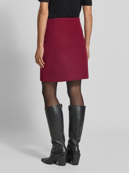 Frauenmodel trägt Ausgestellter Mini-Rock mit Nahtreißverschluss Modell 'FORTUNEALLISON' von VERO MODA in Dunkelrot, glatte Textur, Ganzkörperansicht Rückansicht. Damen Mini-Rock von VERO MODA.