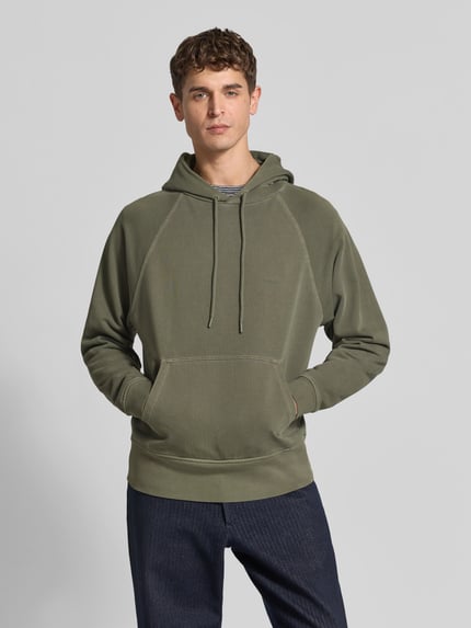Männermodel trägt Regular Fit Hoodie aus reiner Baumwolle von Closed in Olivgrün, Kapuze mit Tunnelzug, Känguru-Tasche, elastische Abschlüsse, krój regular fit, Rückenlänge bei Größe M: 62 cm, Ganzkörperansicht von vorne