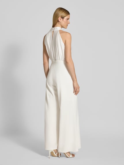 Frauenmodel trägt Jumpsuit mit Schleifen-Applikation von SWING in Weiß, taillierter Schnitt, weites Bein, Cut Out am Rücken, Ganzkörperansicht Rückansicht.