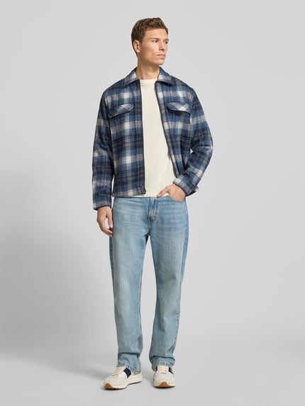 Męski model nosi Hemdjacke mit Reißverschluss od MCNEAL, materiał z dodatkiem wełny, regular fit, niebieska krata, widok całej sylwetki z przodu.