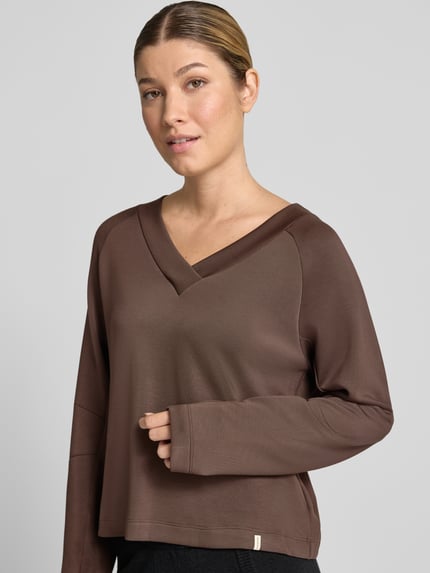 Frauenmodel trägt Regular Fit Sweatshirt mit V-Ausschnitt von SCHIESSER, brauner elastischer Modal-Mix mit Ziernähten, Nahaufnahme Oberkörper.