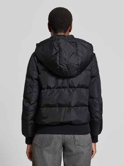 Vrouwenmodel draagt gewatteerd jack met vulling van dons en veren van Armani Exchange in zwart, elastische materiaalmix, regular fit, opstaande kraag, tweewegritssluiting, ritszakken, capuchon, ruglengte maat S 60 cm, schouderbreedte 41 cm, borstwijdte 50 cm, mouwlengte 62 cm, geheel aanzicht rugaanzicht.