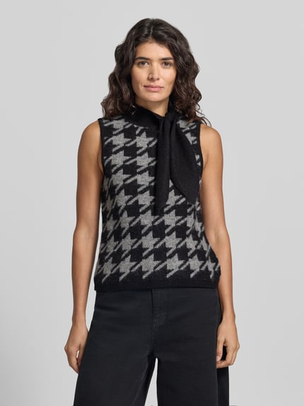Frauenmodel trägt Pullunder mit Schluppe Modell 'VMMARLENA' von VERO MODA mit Hahnentritt-Jacquard in Schwarz-Grau, Strickoptik, Ganzkörperansicht von vorne.