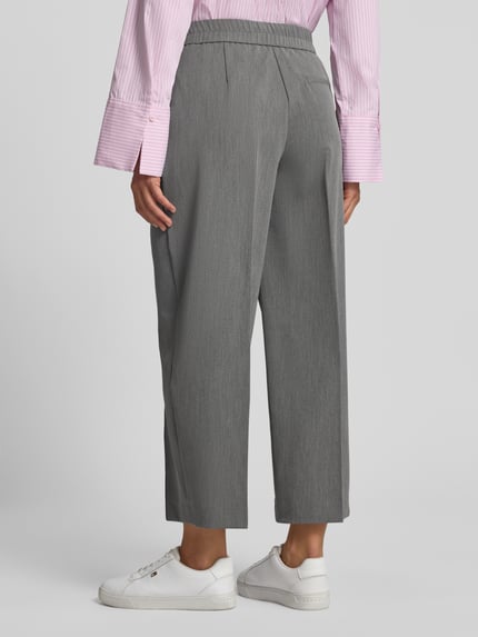 Frauenmodel trägt Stoffhose mit Bügelfalte Modell 'Cisilia' von someday, grauer Material-Mix mit Barrel Fit, Ganzkörperansicht Rückansicht.