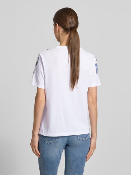 Frauenmodel trägt T-Shirt im Allover-Look mit Pailletten von Marc Cain aus Reine Baumwolle, Regular-Fit, Rundhalsausschnitt, Rückenlänge 59 cm, Ganzkörperansicht Rückansicht.