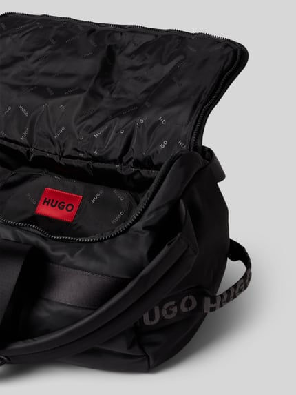 Produktfoto, czarna torba weekendowa Weekender mit Rucksackgurten model 'AYDEN_HOLDALL' od HUGO, z widoczną teksturą tkaniny i czerwonym logo, kontekst: torba weekendowa męska HUGO