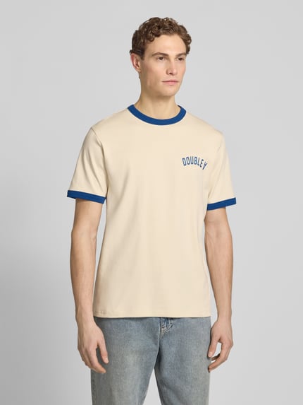 Männermodel trägt T-Shirt mit Rundhalsausschnitt von Wood Wood, cremefarben mit blauen Kontraststreifen, Regular Fit, Ganzkörperansicht von vorne.