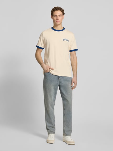 Männermodel trägt T-Shirt mit Rundhalsausschnitt von Wood Wood, reine Baumwolle, Regular Fit, Kontraststreifen, helle Farben, Ganzkörperansicht von vorne.