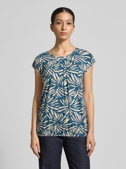 Vrouwenmodel draagt Regular Fit blouse uit viscosemix model 'Minou' van ZABAIONE, all-over bloemenprint, korte mouw, ronde hals, elastische band, ruglengte maat S 62 cm, voorkant volledig zichtbaar, volledige lichaamsaanzicht.