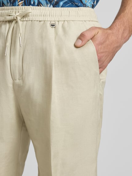 Männermodel trägt Shorts aus Leinen-Viskose-Mix Modell 'NEIL' von Antony Morato, regular fit, lichte beige kleur, detailaufnahme rechter heup, heren shorts met persvouwen, elastische tailleband, context: taillewijdte maat 50: 42 cm, binnenbeenlengte maat 50: 17 cm.
