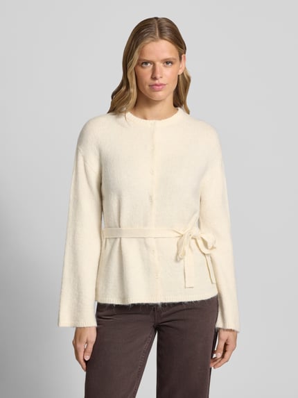 Frauenmodel trägt Cardigan mit Woll-Anteil und Bindegürtel von Gina Tricot, cremefarben, taillierter Schnitt, Knopfleiste, Nahaufnahme Oberkörper.