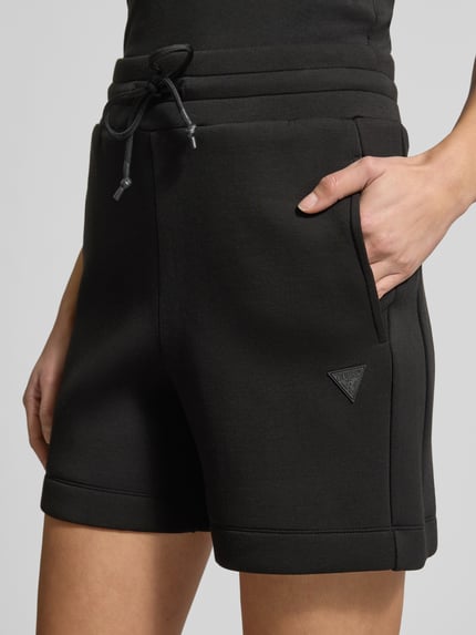 Frauenmodel trägt Regular Fit Shorts aus Viskose-Mix von Guess Activewear in Schwarz mit elastischem Bund und Eingrifftaschen, Nahaufnahme Oberkörper.