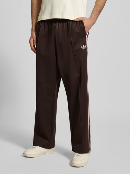 Mężczyzna nosi Straight Fit Sweatpants mit Logo-Stitching Modell 'Firebird' od adidas Originals, bawełniany miks, krój straight fit, z przodu, zbliżenie na nogi.