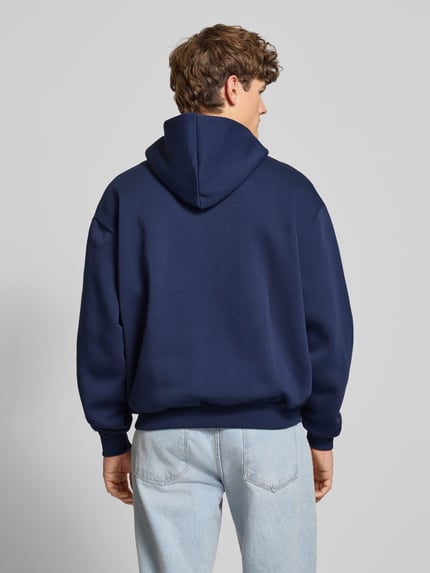Männermodel trägt Hoodie mit Kapuze von KARL KANI aus Baumwoll-Mix in Dunkelblau, lockerer Schnitt, gerippte Abschlüsse, Ganzkörperansicht Rückansicht.