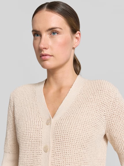 Frauenmodel trägt Cardigan mit V-Ausschnitt Modell 'Temmy' von Someday in Beige, Material-Mix mit Baumwoll-Anteil, Knopfleiste, 1/2-Arm, Regular-Fit, Nahaufnahme Oberkörper.