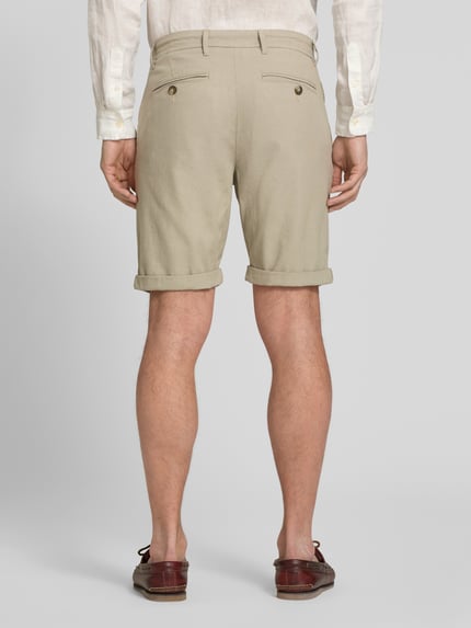Männermodel trägt Slim Fit Chinoshorts aus Baumwoll-Mix Modell 'LUTON' von SELECTED HOMME, beżowy, gładki, krój slim fit, tylne kieszenie z guzikiem, drobna tkana faktura, widok całej sylwetki z tyłu.