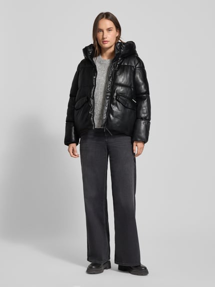 Frauenmodel trägt schwarze Steppjacke mit Kapuze Modell 'AURORA' von khujo, Regular-Fit, Reißverschluss, Pattentaschen, Label-Detail, Ganzkörperansicht von vorne. Rückenlänge 65 cm, Schulterbreite 44 cm, Brustweite 50 cm, Ärmellänge 60 cm.