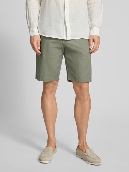 Mężczyzna nosi Regular Fit Bermuda aus Leinen-Baumwolle-Mix von Tom Tailor Denim w kolorze oliwkowym, z przodu kieszenie, z tyłu kieszenie z lamówką, materiał lniano-bawełniany, widok całej sylwetki z przodu.