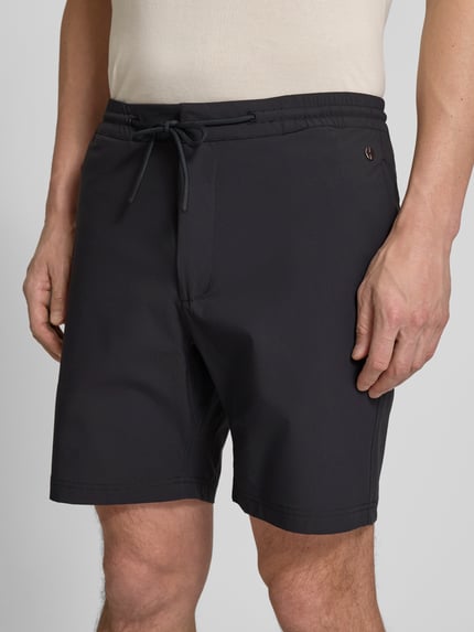 Mężczyzna nosi Straight Fit Shorts mit Eingrifftaschen Modell 'Drift' od SCANDINAVIAN EDITION, czarne, elastyczny materiał, z przodu, zbliżenie na górną część.
