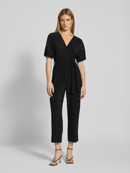 Modelka nosi Regular Fit Jumpsuit mit V-Ausschnitt Modell 'Olinda' od YAS, czarny plisowany, pasek, damski, krótki rękaw, widok całej sylwetki z przodu. Szerokość w rozmiarze 36: 30 cm, długość tyłu: 74 cm, długość rękawa: 15 cm, długość całkowita: 143 cm, długość nogawki: 66 cm, krój regular fit.