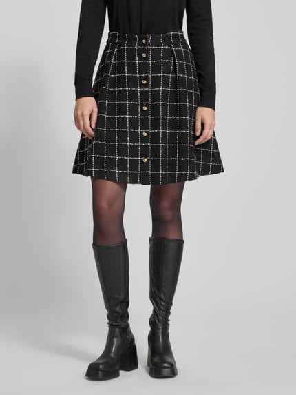 Kobiece modelka nosi czarną spódnicę mini w kratę z guzikami, Ausgestellter Mini-Rock mit Viskose-Anteil Modell 'RIKLA-1' od HUGO, tkanina bouclé, jednolity wzór, widok całej sylwetki z przodu.