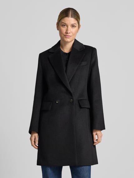 Frauenmodel trägt Regular Fit Mantel mit Reverskragen Modell 'DALI' von MANGO in Schwarz, Zwei-Knopfleiste, glatte Oberfläche, Ganzkörperansicht von vorne. Rückenlänge 93 cm, Schulterbreite 38 cm, Brustweite 47 cm, Ärmellänge 60 cm.