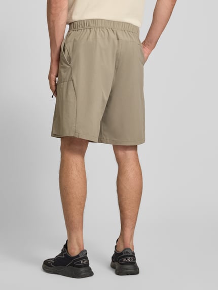 Männermodel trägt Relaxed Fit Cargoshorts mit Label-Schriftzug Modell 'GLOBE CARGO' von BOSS Green, unifarben, elastischer Bund, Ganzkörperansicht Rückansicht.