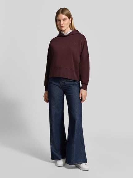 Frauenmodel trägt Sweatshirt mit Kapuze und Label-Detail von MARC O'POLO in Unifarbe, Jersey, lange überschnittene Ärmel, Ganzkörperansicht von vorne.