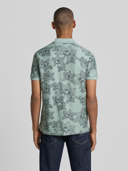 Männermodel trägt Slim Fit Poloshirt mit floralem Allover-Print von Lerros aus Reiner Baumwolle, hellgrün mit Polokragen, Ganzkörperansicht Rückansicht.